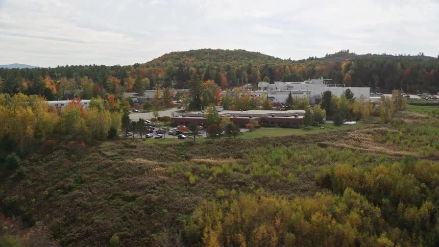 An aerial view of a building with cars parked next to a highway and amidst coniferous trees