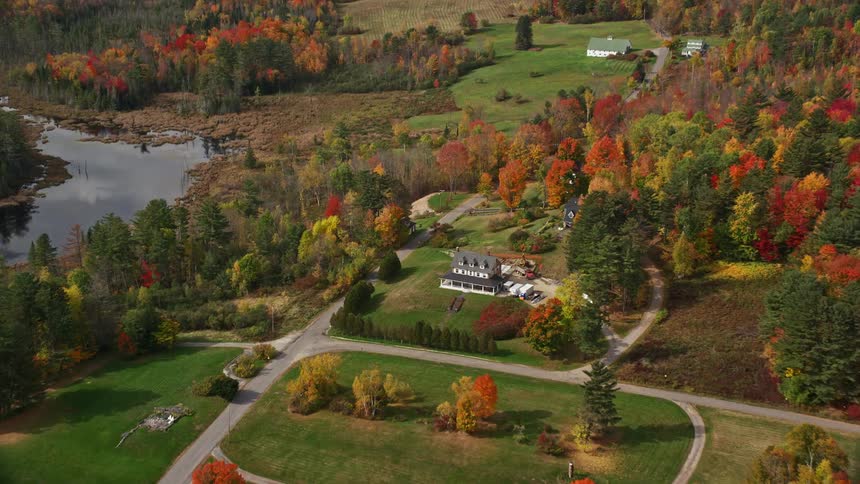 A large house in a rural region with many trees around and a lake nearby