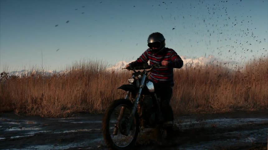 A man riding a dirt bike through wetlands with white mountains in the background