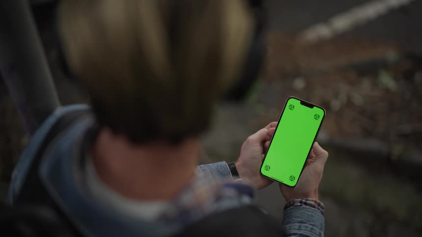 Overtheshoulder view of a man with headphones looking at an iphone and looking suspiciously to the side