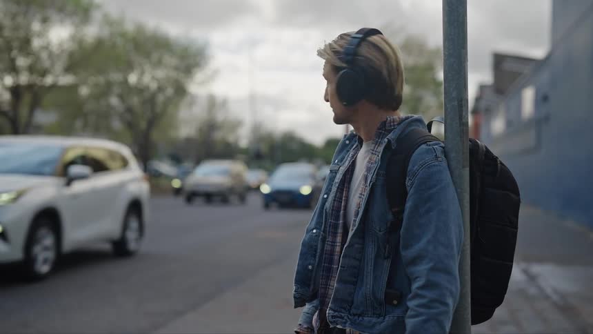 Man wearing headphones checks wristwatch while waiting near busy street