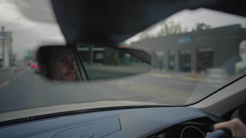A man driving a car and looking in the rear view mirror