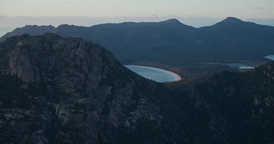 An aerial panorama of mountains surrounding a beach under a dawn sky