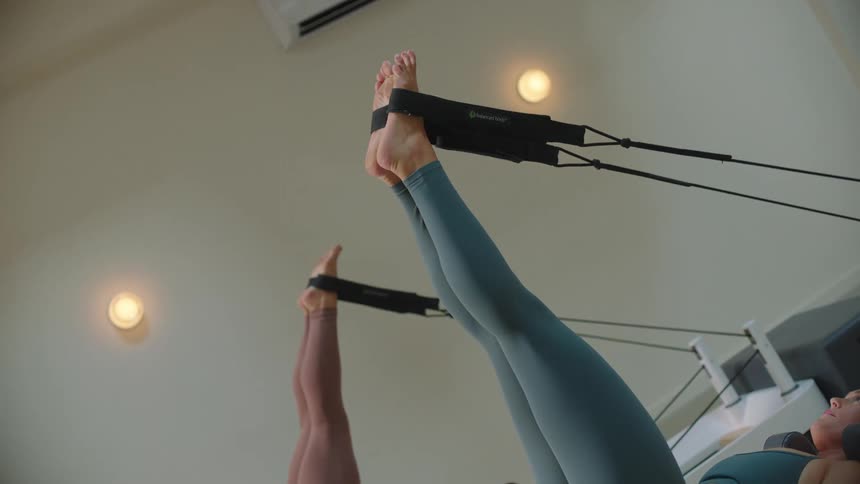 Two women lying on pilates equipment using an elastic band for stretching