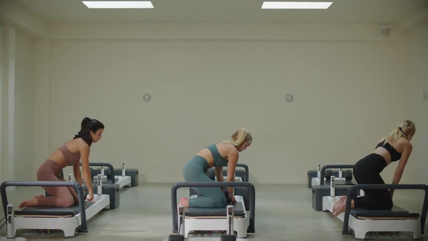 Three ladies stretches kneeling on gym equipment while another lady gives them instructions