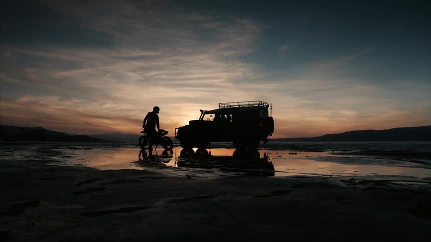 A man has a dirt bike near a truck by the water