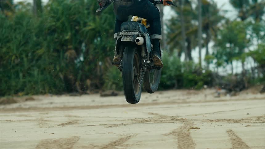 A man does a jump in the sand on a dirt bike