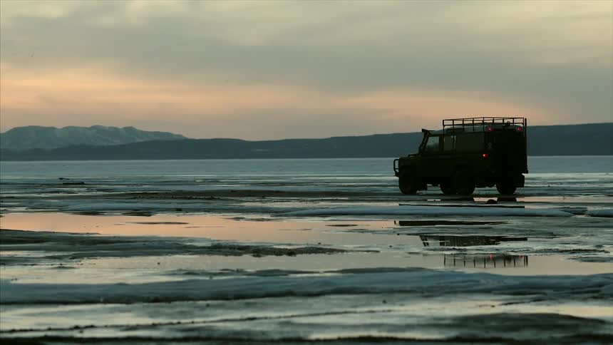 A truck riding down an empty beach at sunset