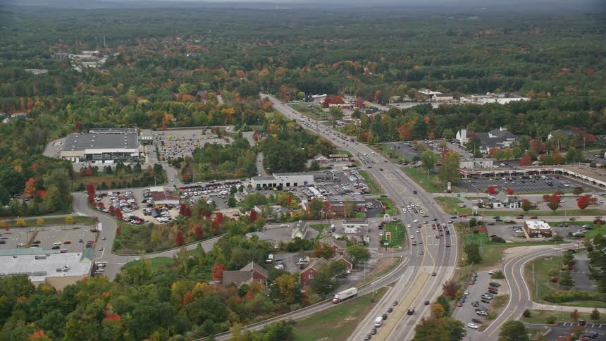 Traffic flows along highways through town surrounded by woods during the fall