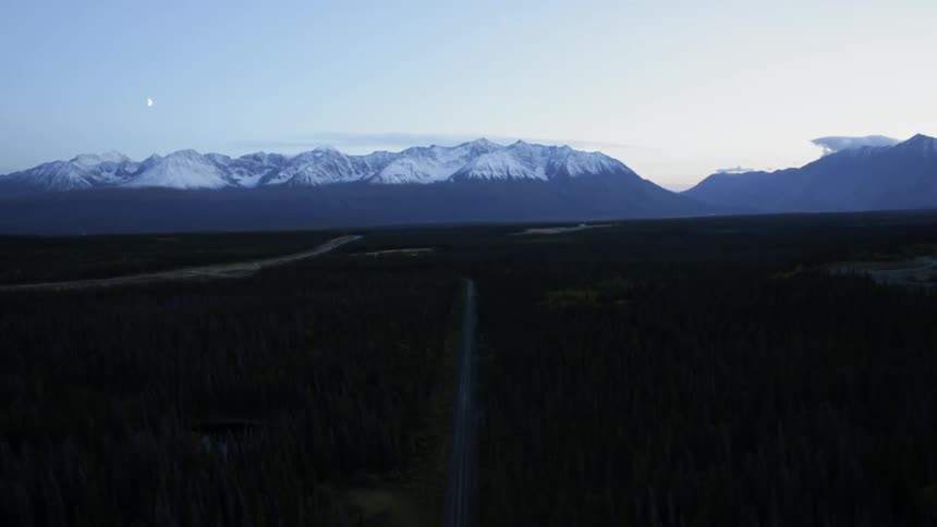 A dirt path through a large field with mountains in the background