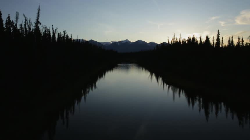 Smooth waters through some plants heading towards the mountains