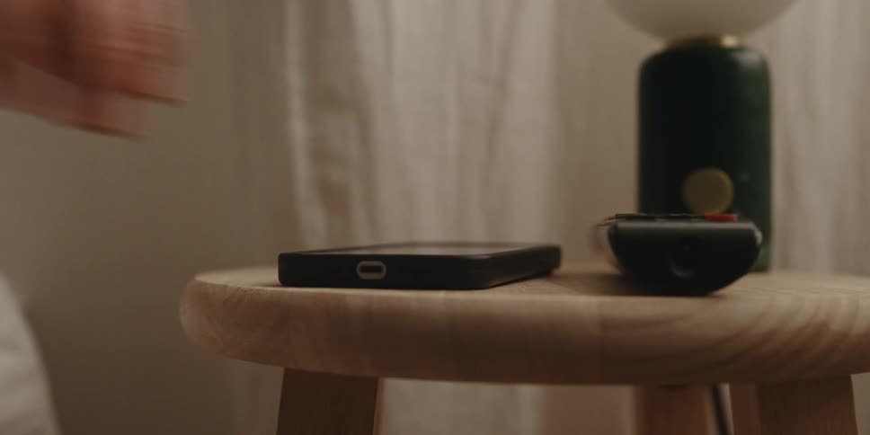 A man picks up his smart phone from atop a wooden stool
