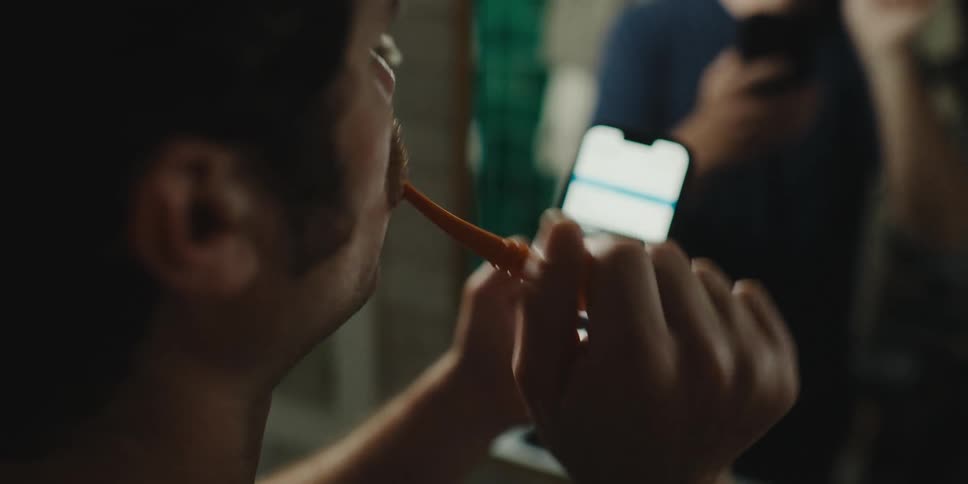 Man brushing his teeth while looking at his cell phone