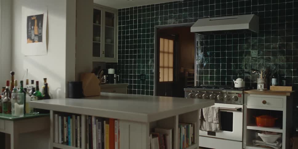 Kitchen interior with dark tile backsplash white cabinets and a cooking rangea kitchen island with books and bottles is in the foreground