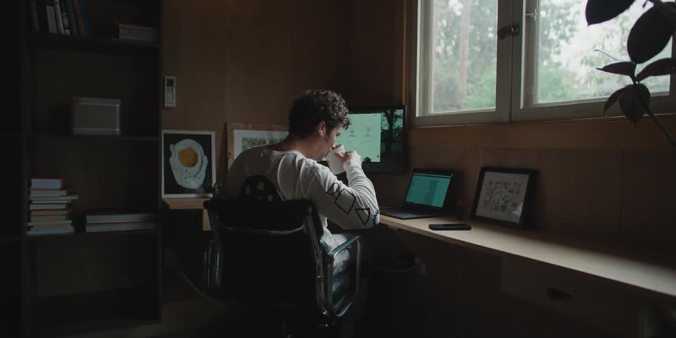 A man sitting at his laptop computer pauses to take a drink from his coffee mug