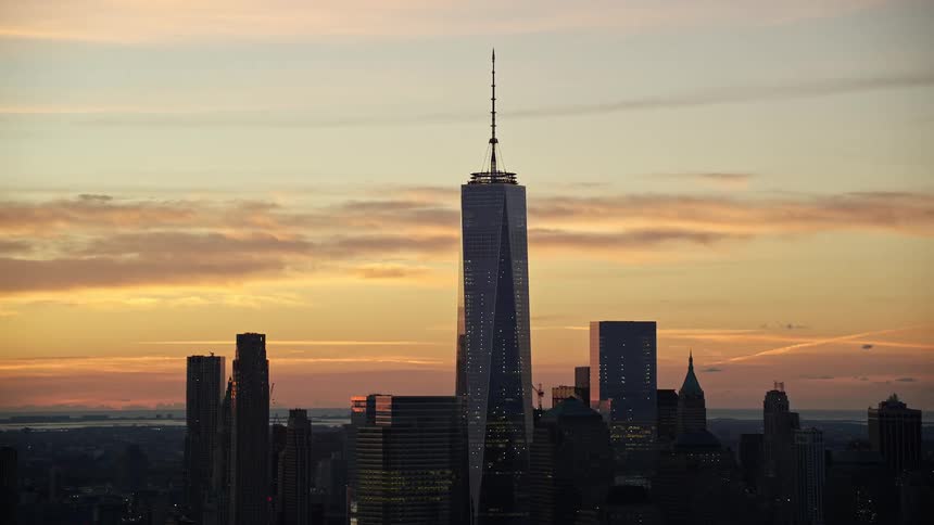Aerial view of a sunset silhouette of a city skyline with a tall skyscraper dominating the scene against a cloudy sky