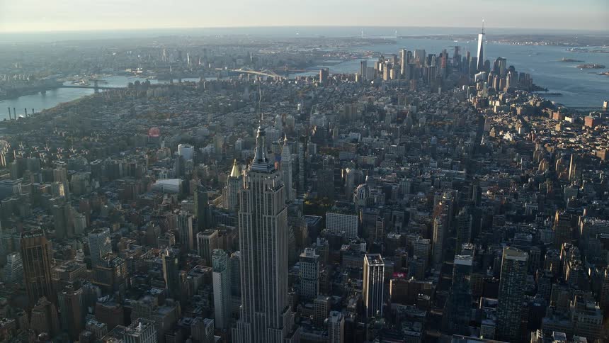 Aerial view of a dense urban skyline with buildings of various sizes and prominent skyscrapers with sea in the distance