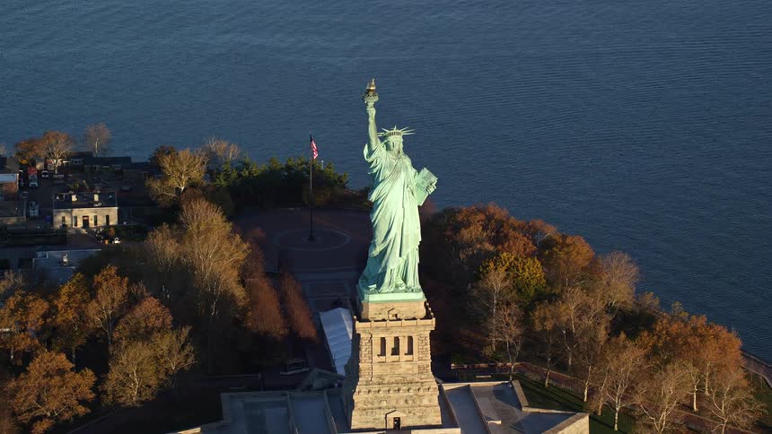 An aerial view of the statue of liberty with its coppergreen patina gleaming in the sunlight on liberty island and the cityscape of manhattan stretches out in the distance