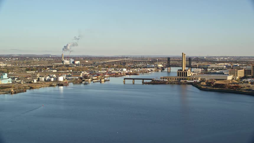 Clear daytime view across a river towards an industrial district with active smokestacks a bridge spanning the river and various buildings