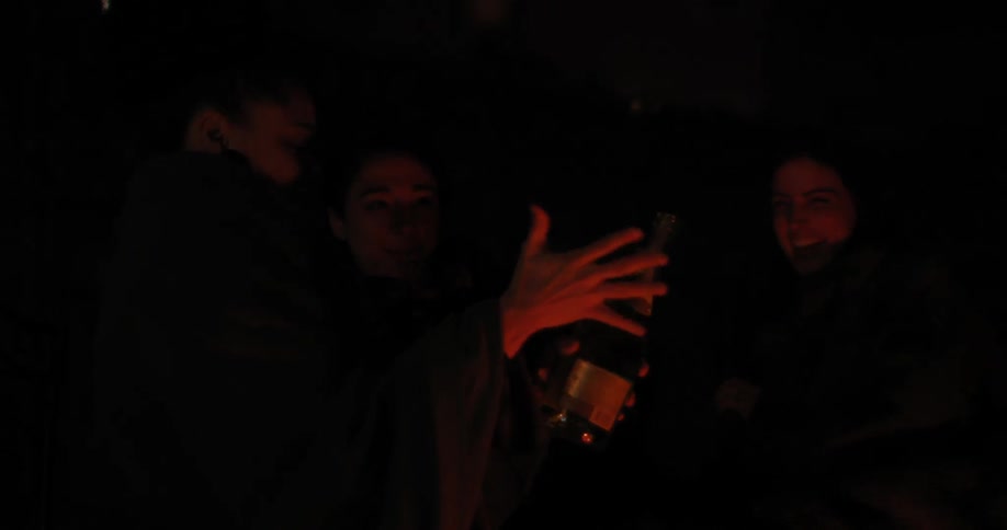 People open a bottle at night near a campfire