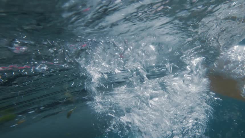 View from inside the sea of a canoe passing by with the paddler creating bubbles and pressure in the water
