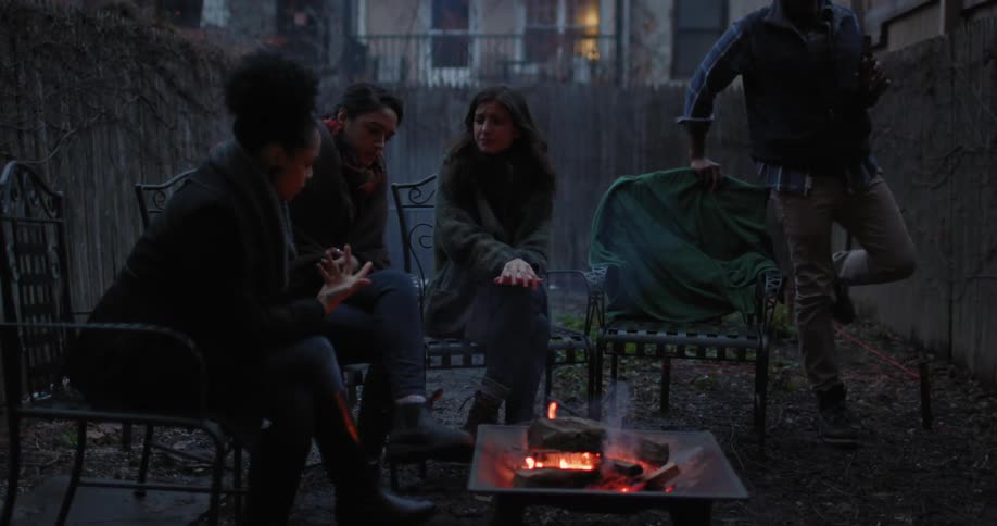 People sit around a fire in a yard talking