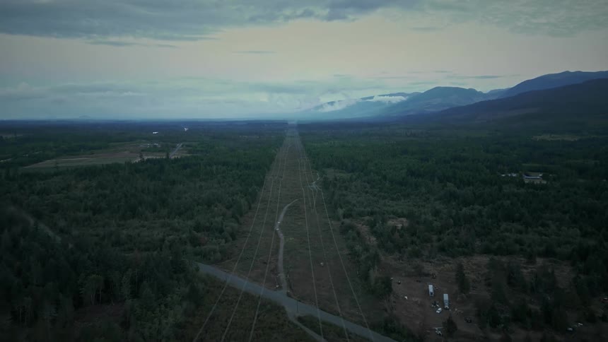 Vehicles park in field near intersection between stream and highway on cloudy day
