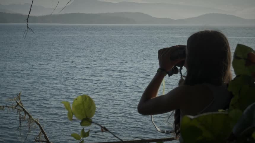 A young girl is using binoculars to look at the sea