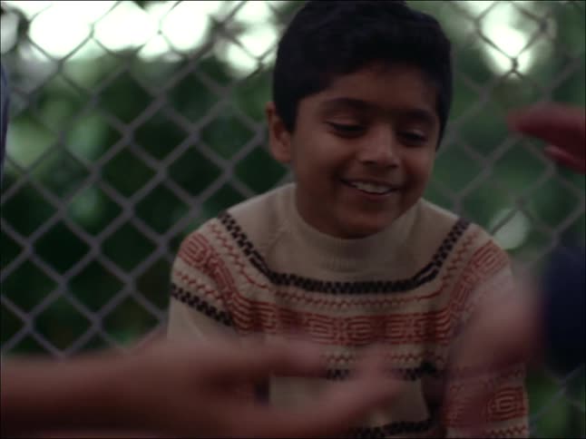 Children playing on another and laughing next to wire netting fence