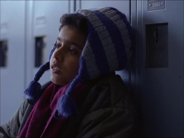 Portrait of a boy sitting and leaning against school lockers with a sad facial expression