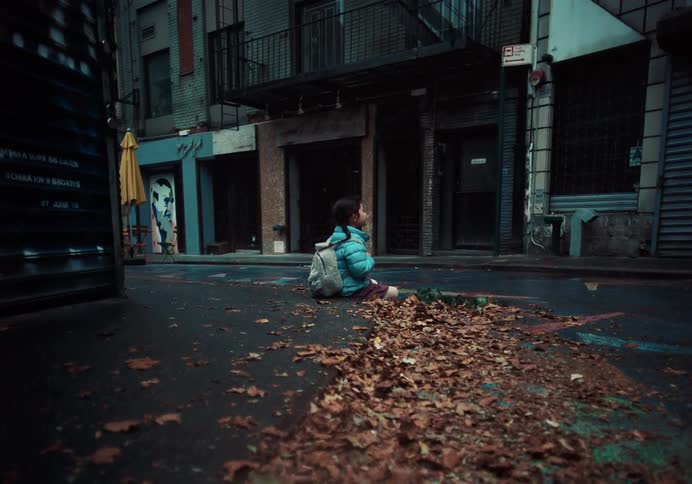 Lonely Asian American Child Sitting in Empty Urban Street Amid Fallen Leaves