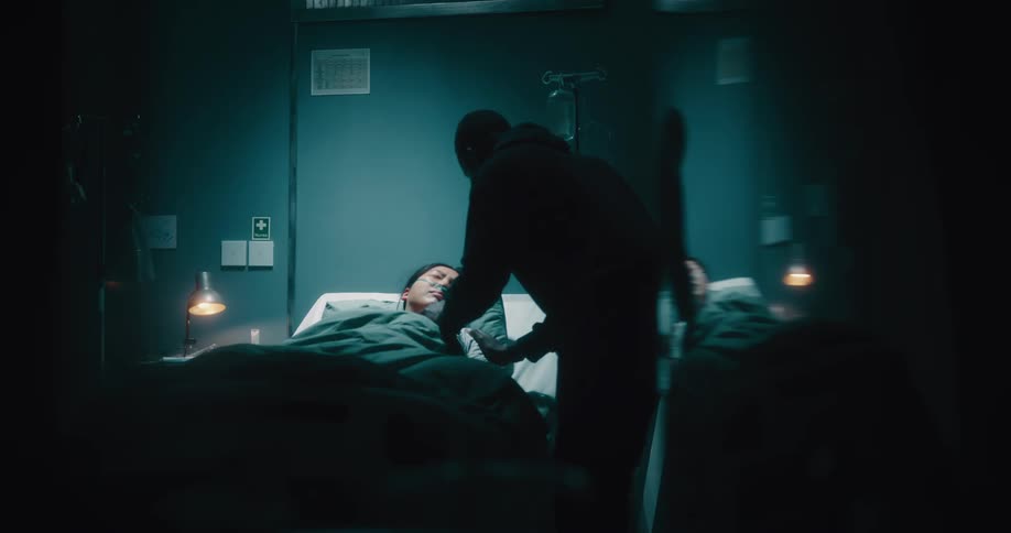 A man affectionately tends to a female patient with a nasal cannula lying in a hospital bed