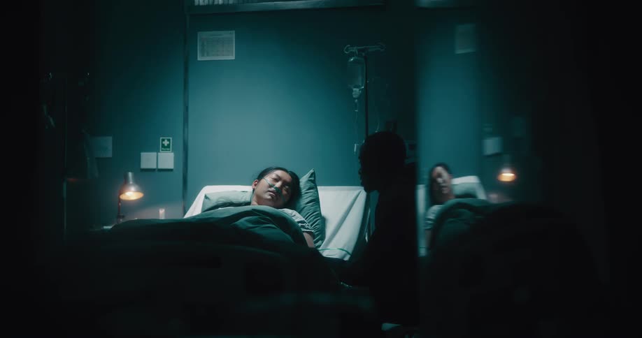 Lady on the hospital bed talking with a black man seated near the bed