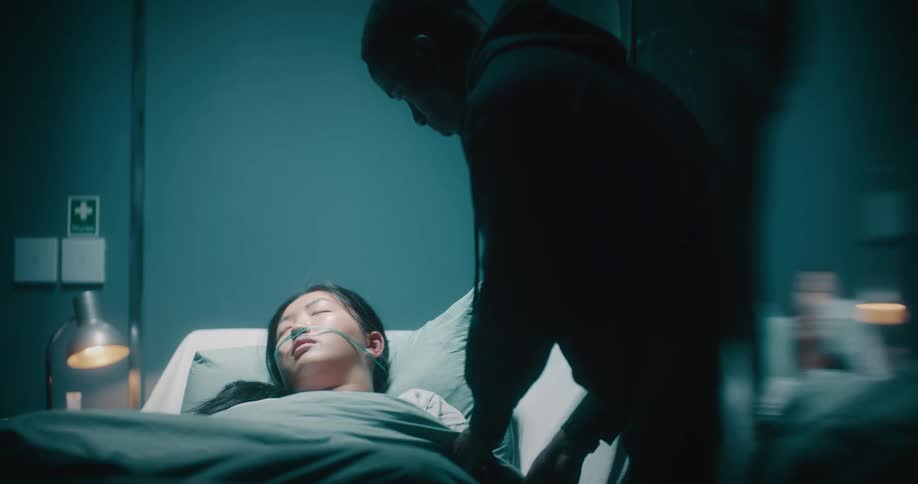 A man adjusting the covers of his partner who is lying on a hospital stretcher and caressing her face
