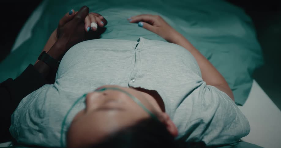 Woman lying on the hospital stretcher receiving a caress on her head and hands from her partner