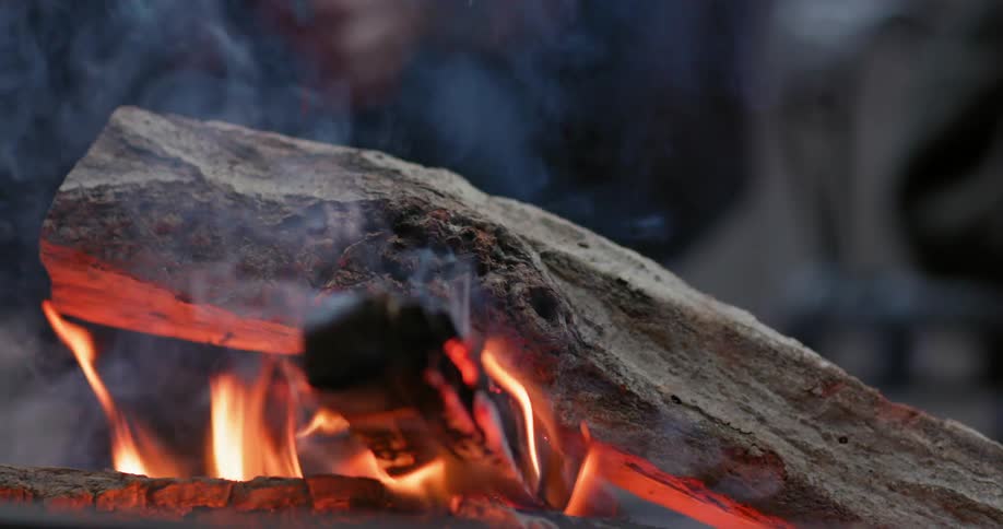 A person puts a log on a campfire