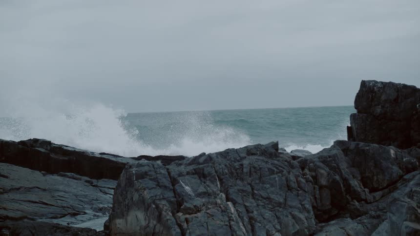 Waves crash over the rocks on a cloudy day