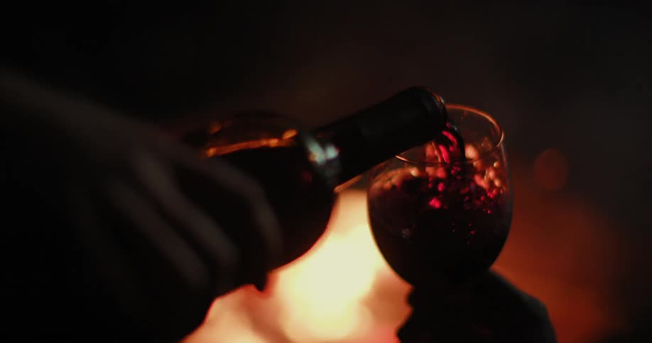 A person is filling a glass with wine by a fire