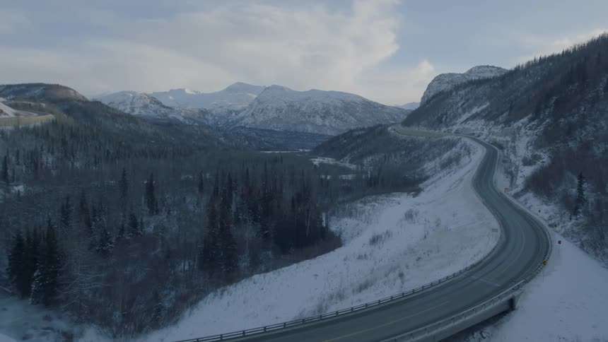 Pullback reveal of a curved bridge along a mountain valley highway