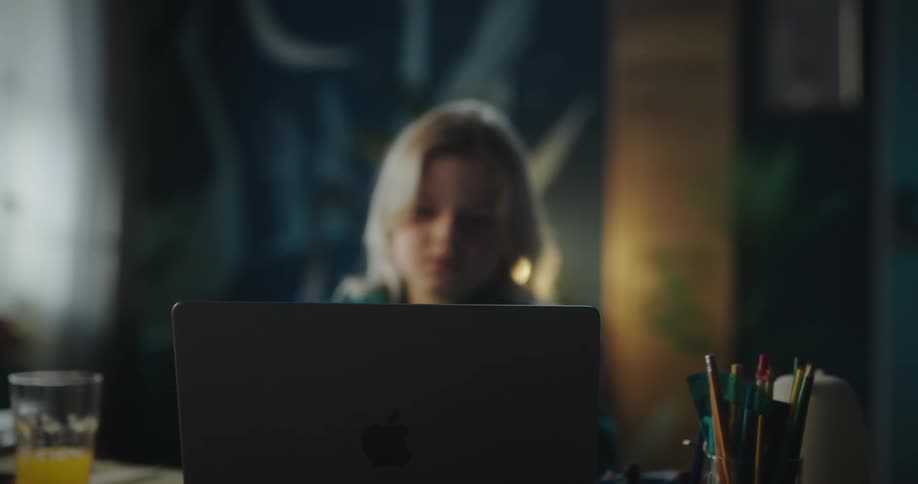 Blonde girl sitting at table looks at laptop in her room