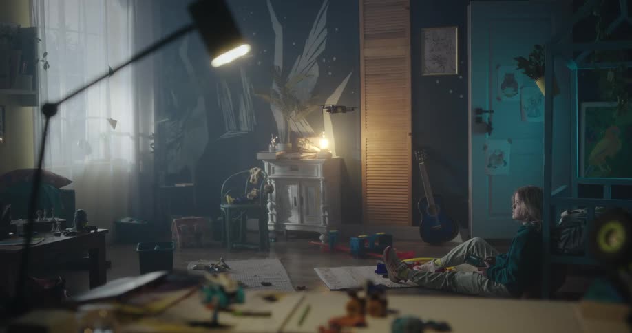 A female child seated on the floor while flying a drone inside a room