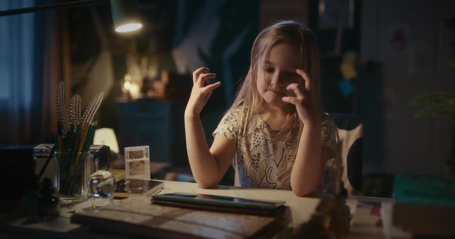 Portrait of a little girl sitting at a table playing with a tablet and getting frustrated