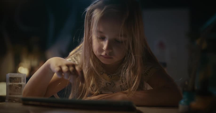 A blonde girl sits at table using a tablet