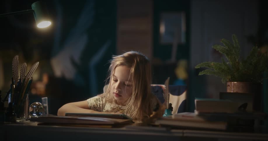 A little girl is sitting at a desk playing with a tablet computer