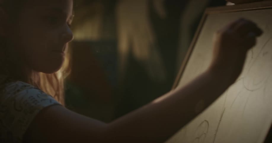 Girl focused on drawing on a blackboard in a room softly illuminated by natural light