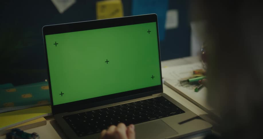 A hand is on the keyboard of a laptop computer with a green screen