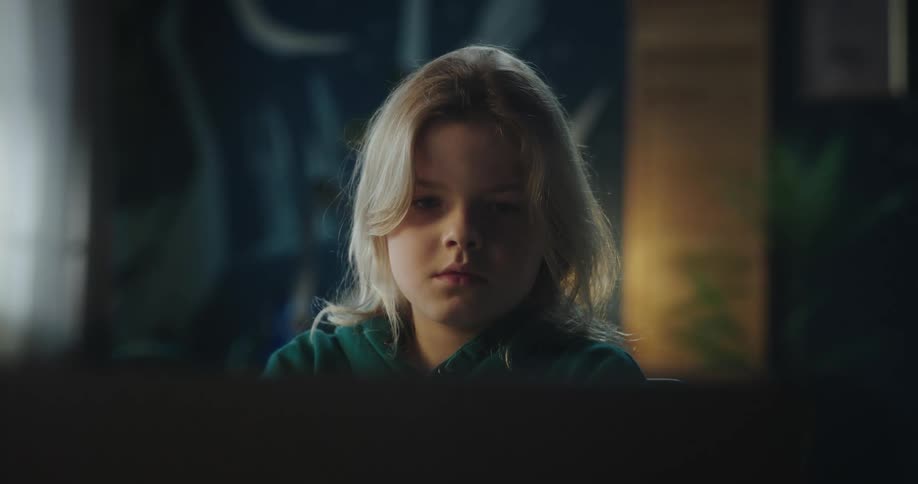 A girl is sitting at a desk behind a laptop computer