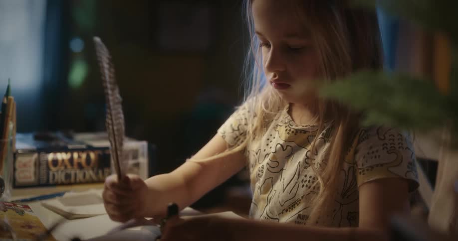 A girl with blonde hair opens a notebook and prepares to write using a feather
