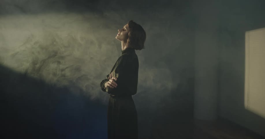 Woman stands in a room filled with smoke under moving lights