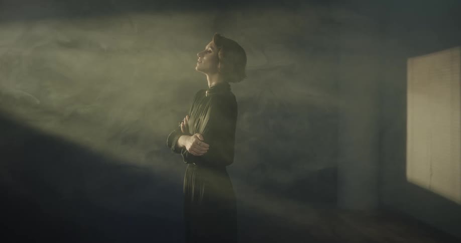 Sunlight streaming through windows onto a woman wearing a black dress standing with arms crossed